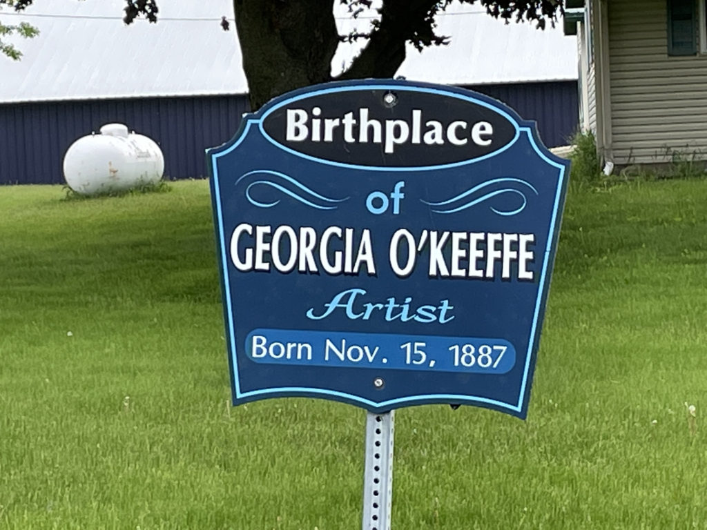 Small blue sign on a silver post marking the birthplace of Georgia O'Keeffe